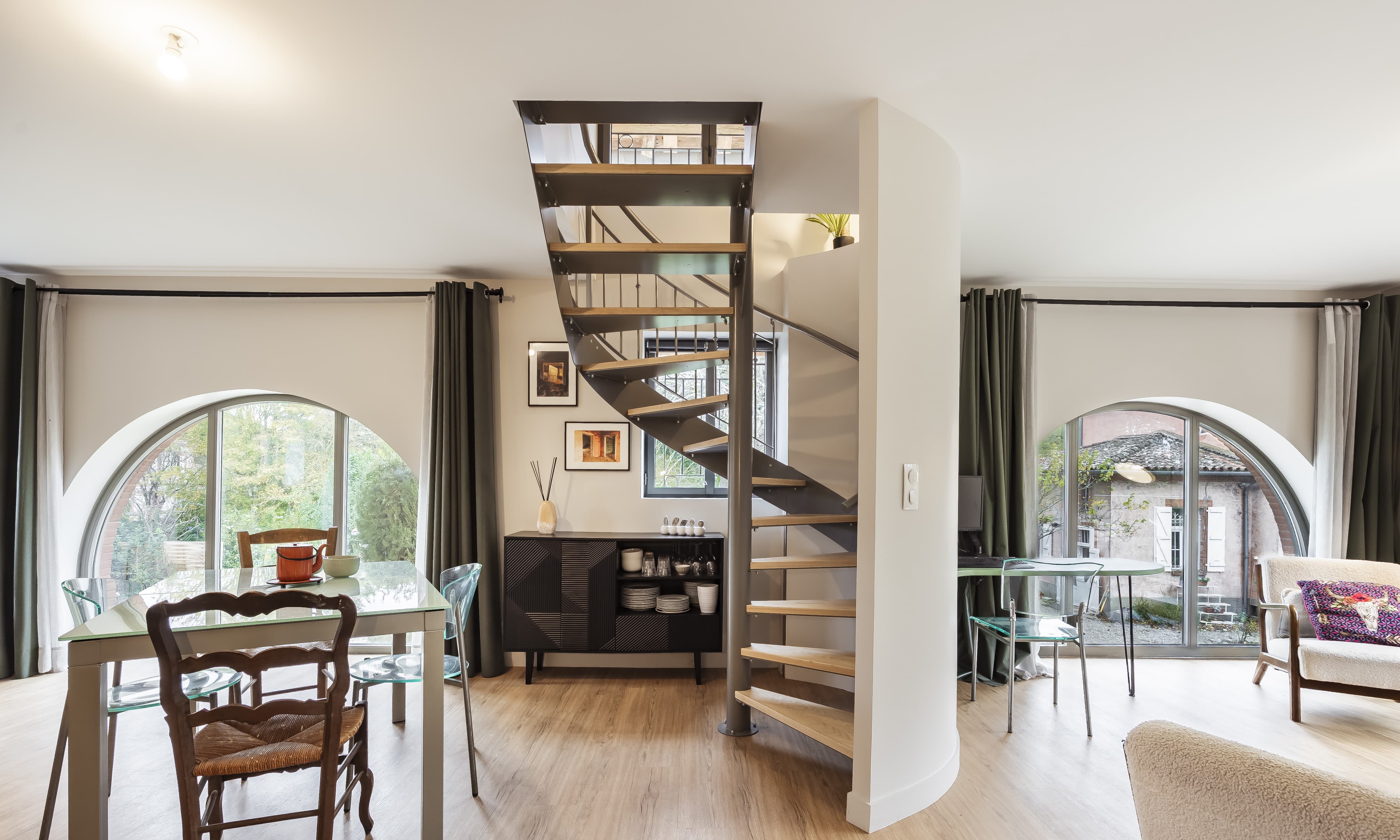 Séjour lumineux avec escalier hélicoïdal en acier et grandes baies cintrées ouvertes sur le parc