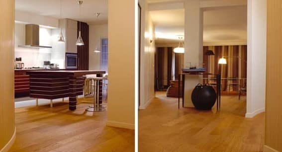 Vue traversante de la cuisine en bois sombre vers le séjour en enfilade, baigné de lumière sur un parquet de chêne clair