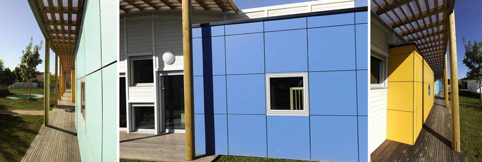 Coursive couverte par une pergola bois le long des façades en panneaux bleus et jaunes, ouverte sur le jardin